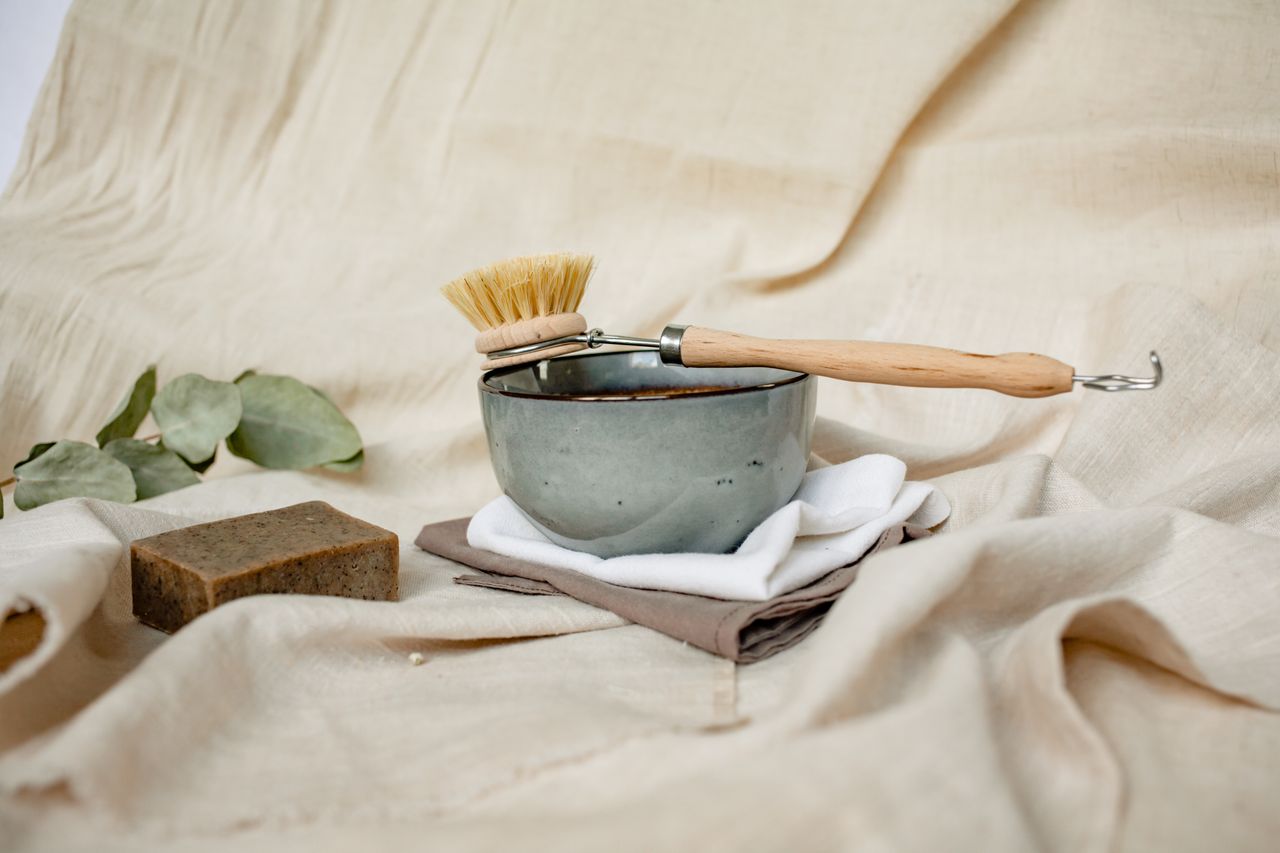 Eco-friendly cleaning set featuring a ceramic bowl, brush, soap, and natural linens with eucalyptus leaves.