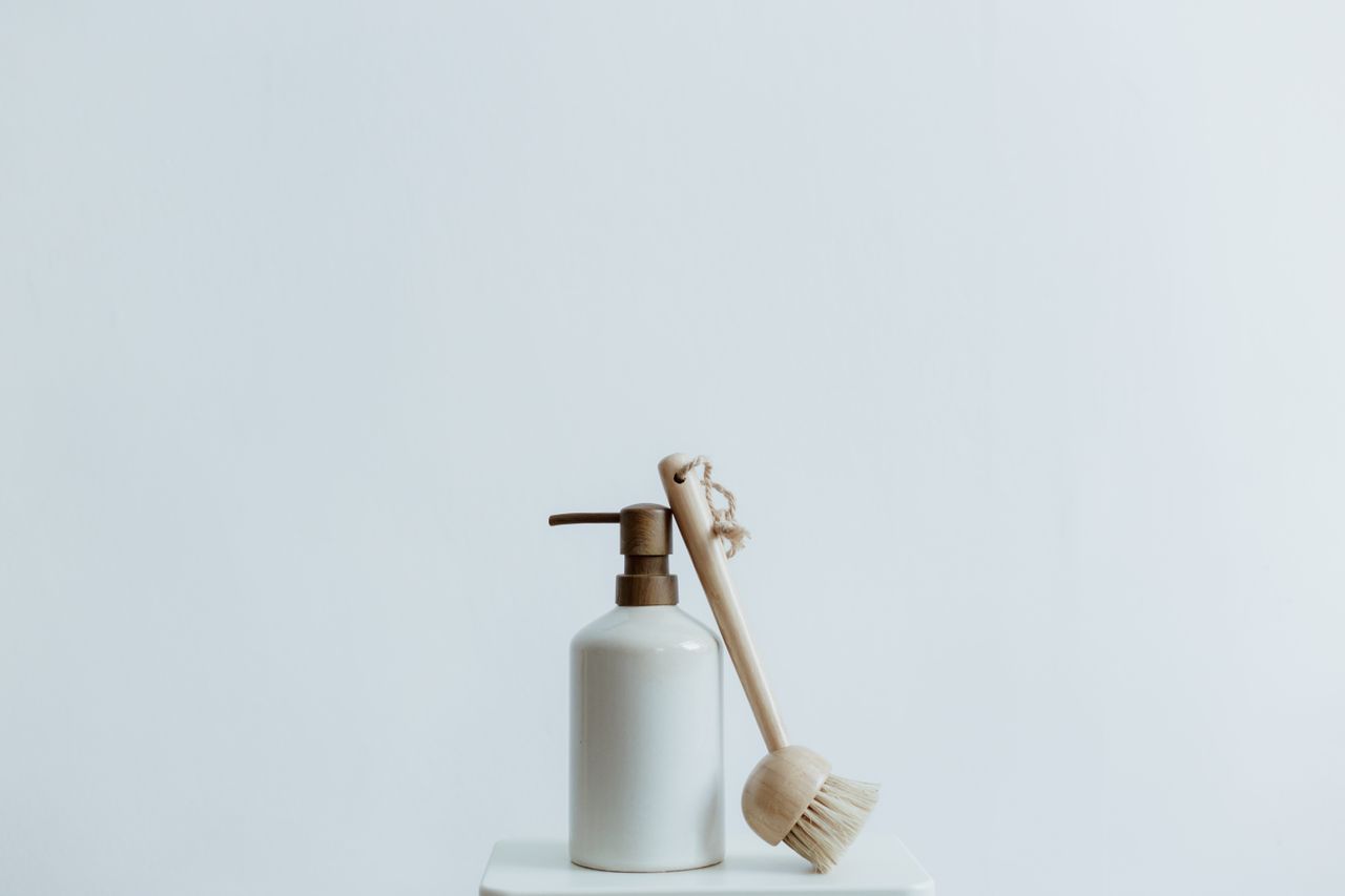 about-img-01 A minimalist soap dispenser and wooden brush set against a plain white background.